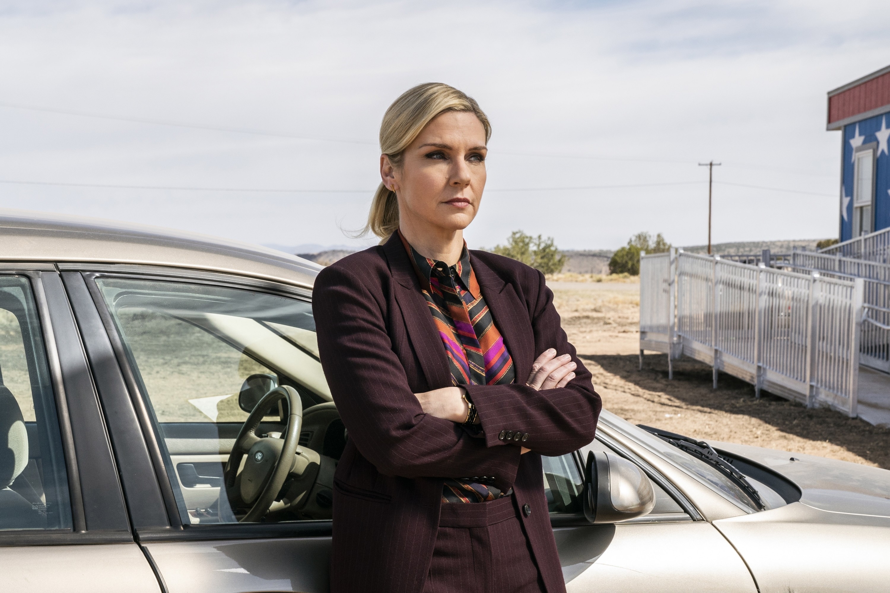 Woman in a business outfit standing by a car with arms crossed