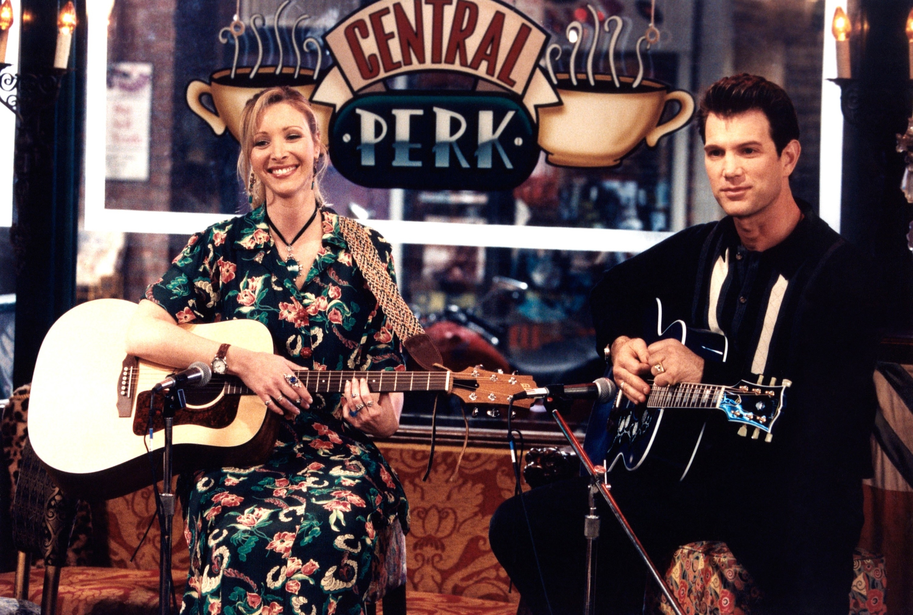 Phoebe and guest playing guitars in Central Perk from &quot;Friends.&quot; Phoebe wears a bohemian style dress