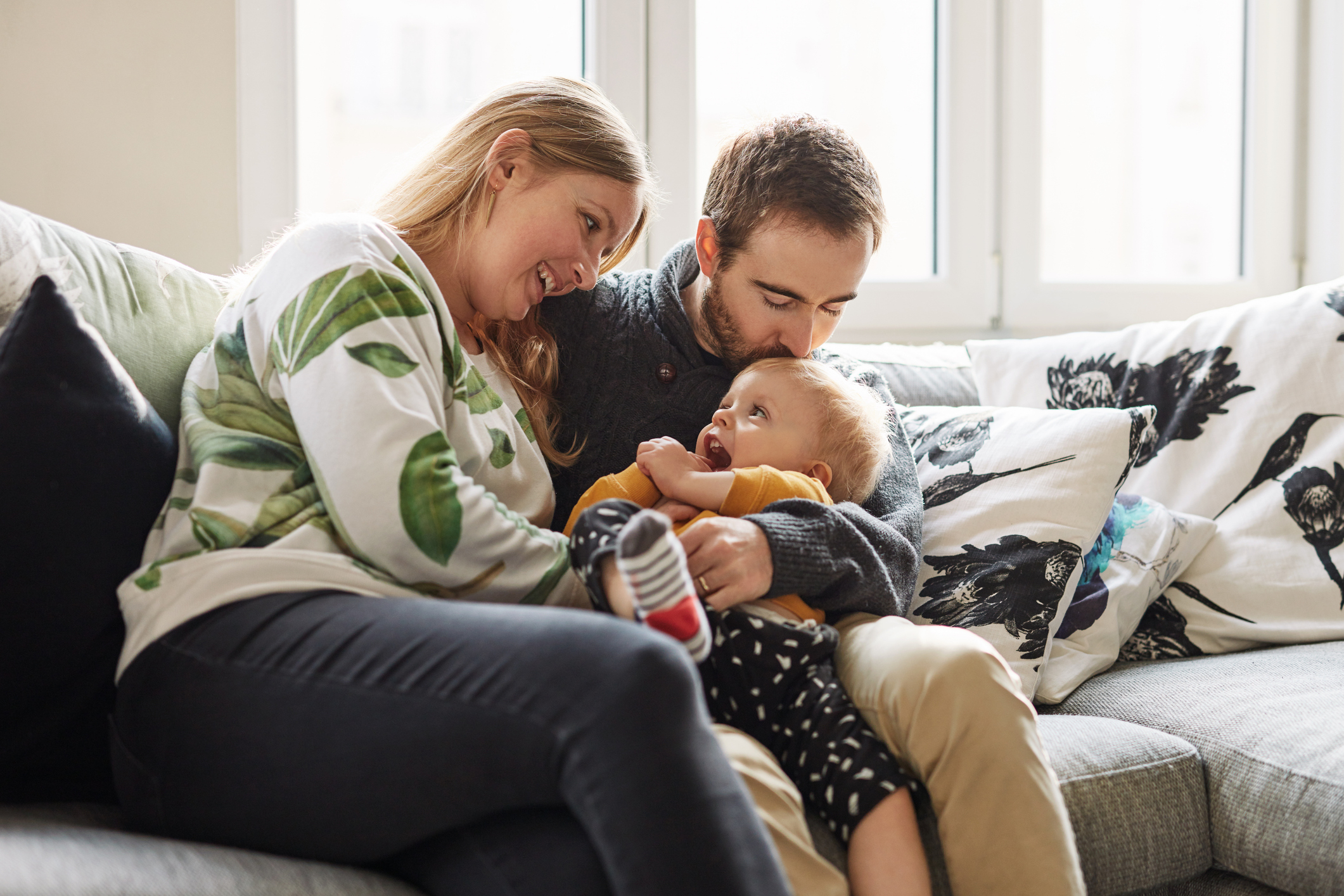 Couple and baby sitting on sofa, sharing a joyful moment, suggesting family intimacy and love