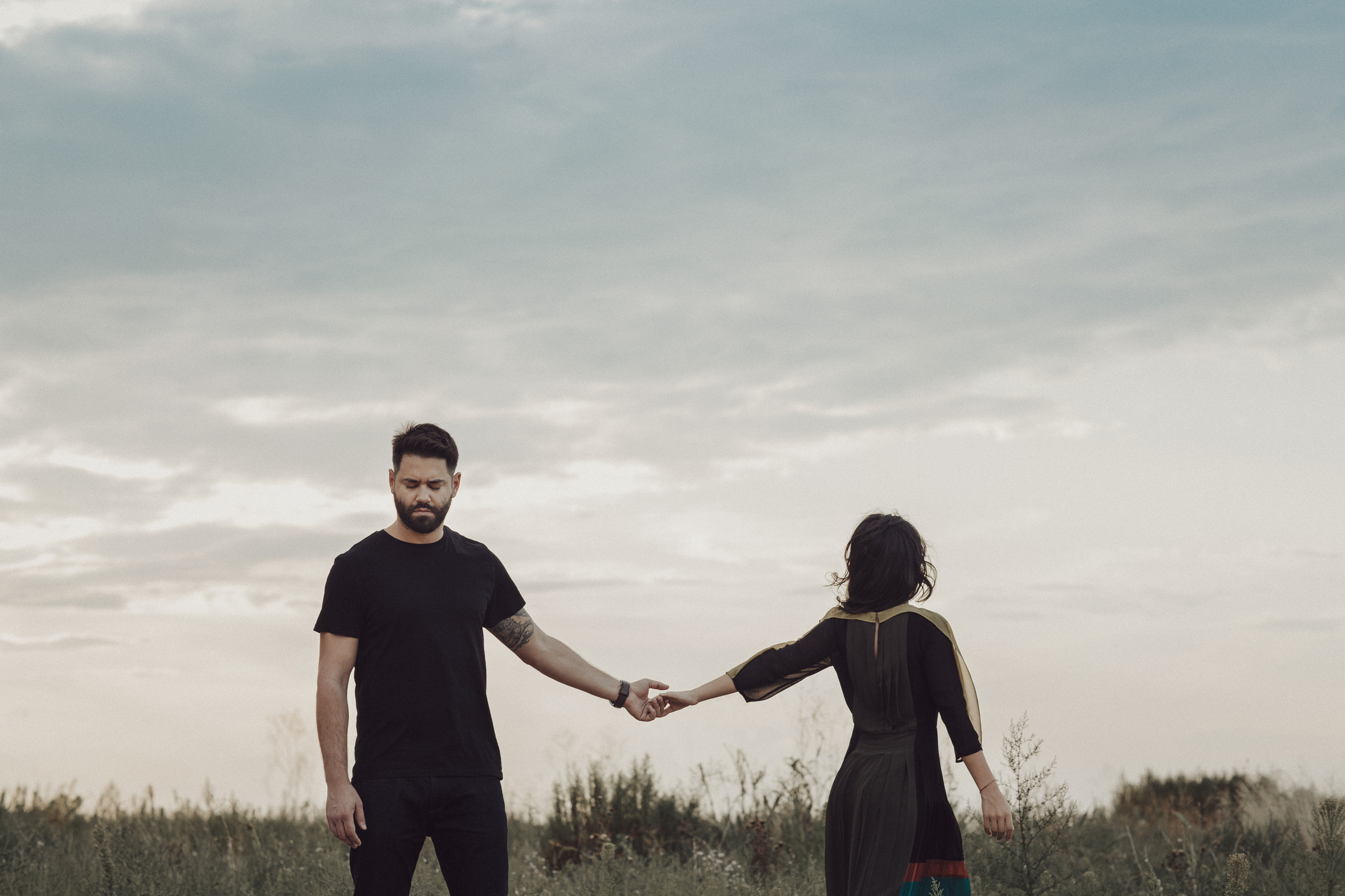 Couple holding hands in a field, facing away from the camera