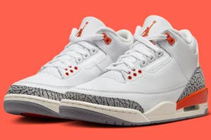 A pair of white Air Jordan 3 sneakers with orange accents and elephant print detailing