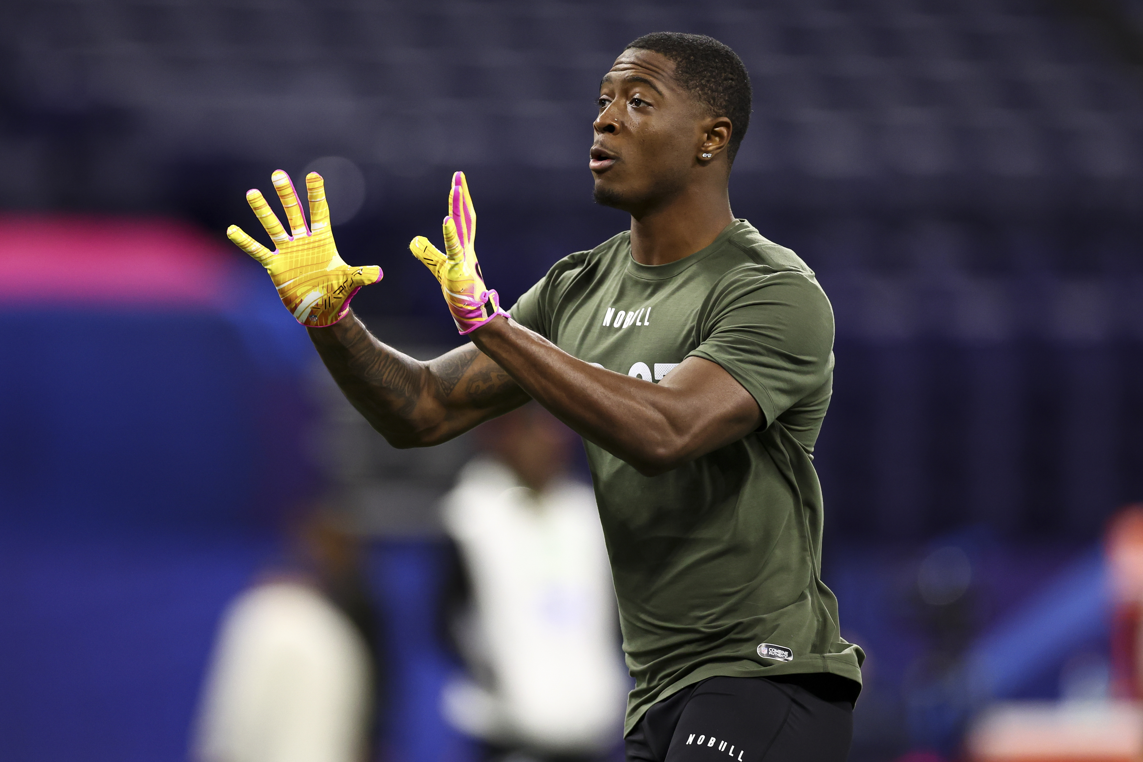 Football player in a workout shirt and gloves catches a pass during pre-game warm-up