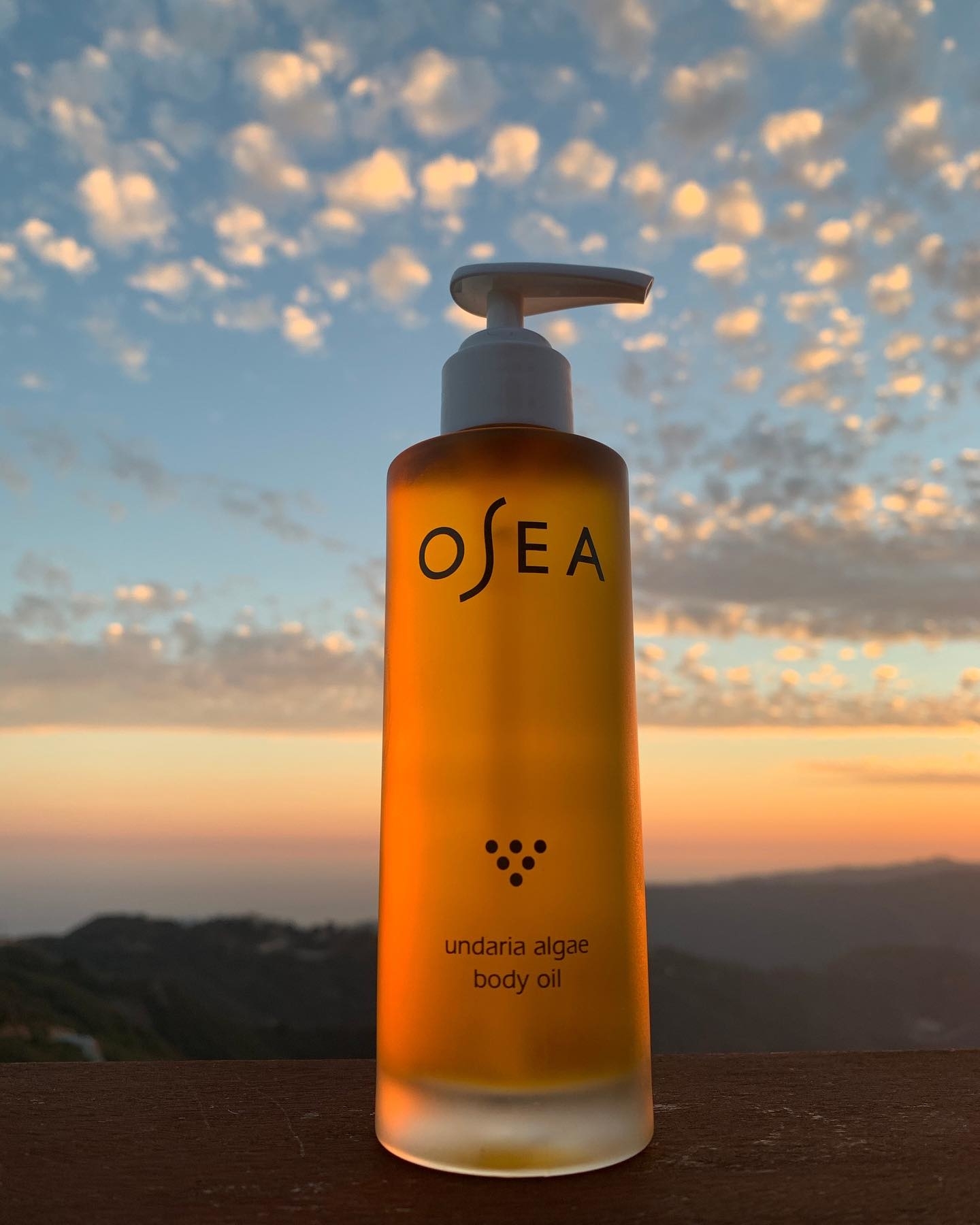 OSEA body oil bottle in front of a sunset sky