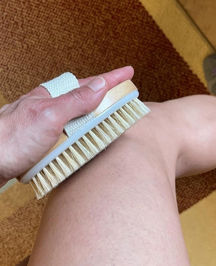 Person using a dry brush on their leg for skincare