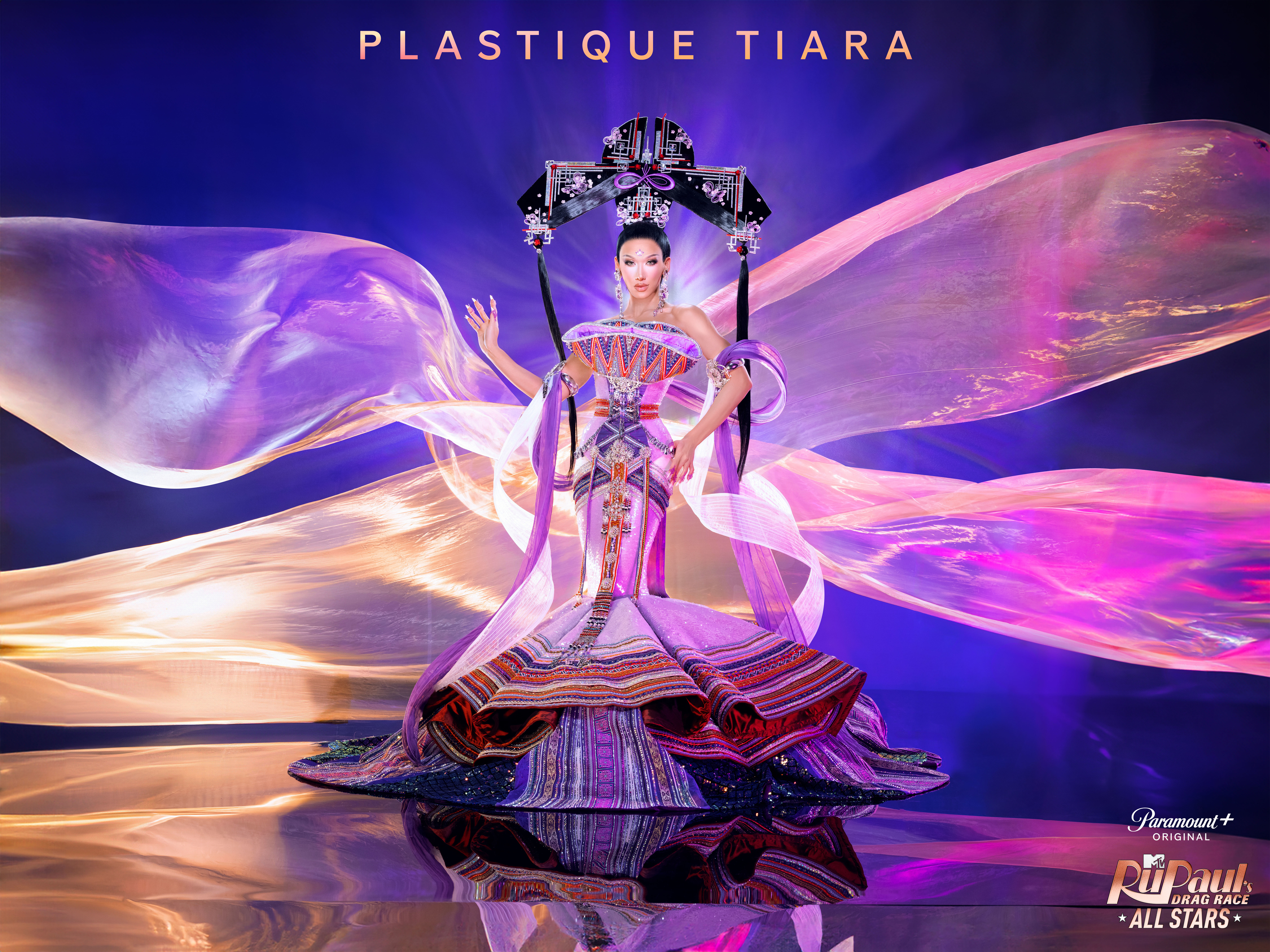 Plastique Tiara in an elaborate costume with flowing sleeves and a tiered skirt on a stage