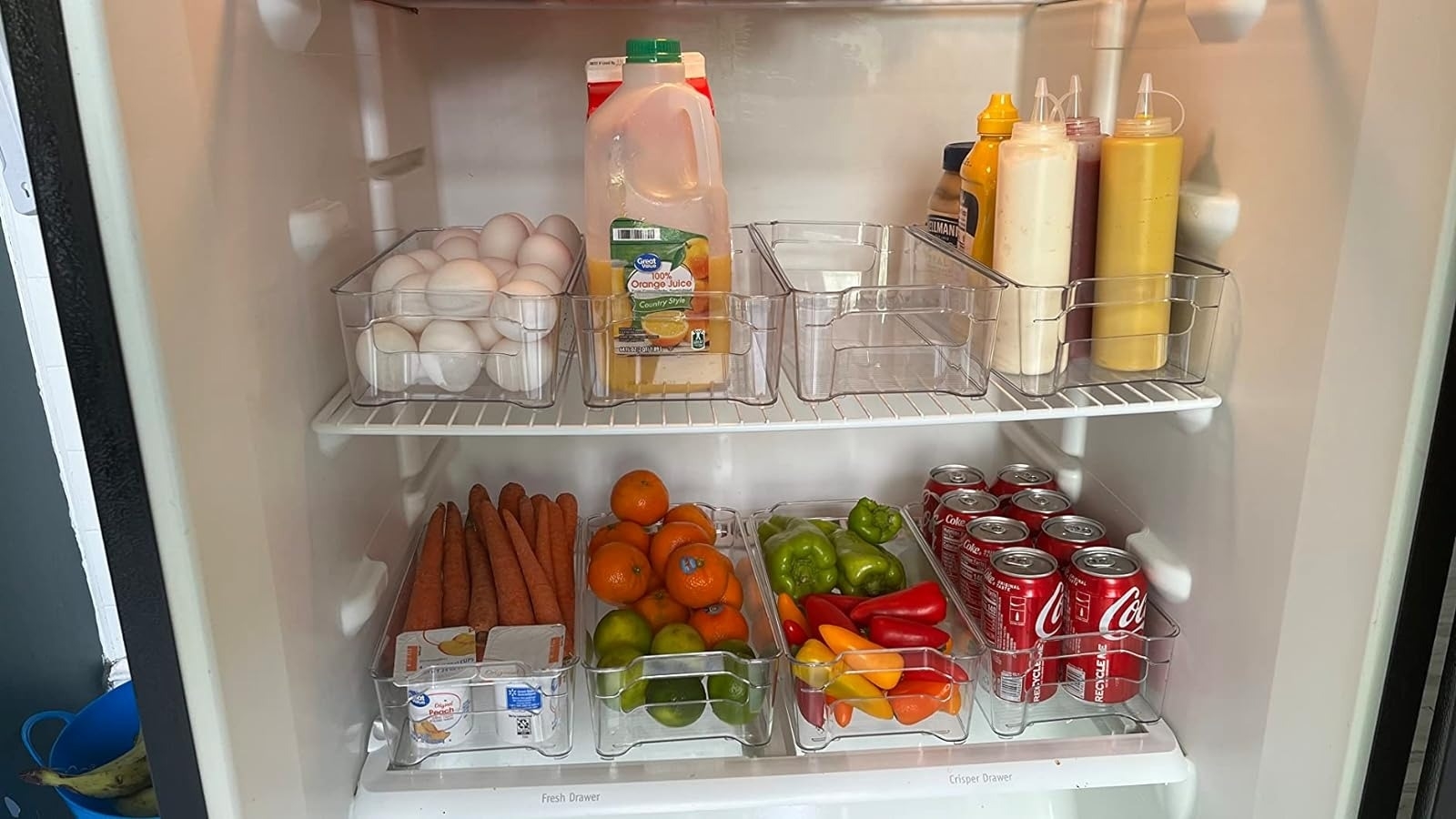 Organized fridge interior with clear storage bins containing drinks, fruits, and dairy products for efficient space use