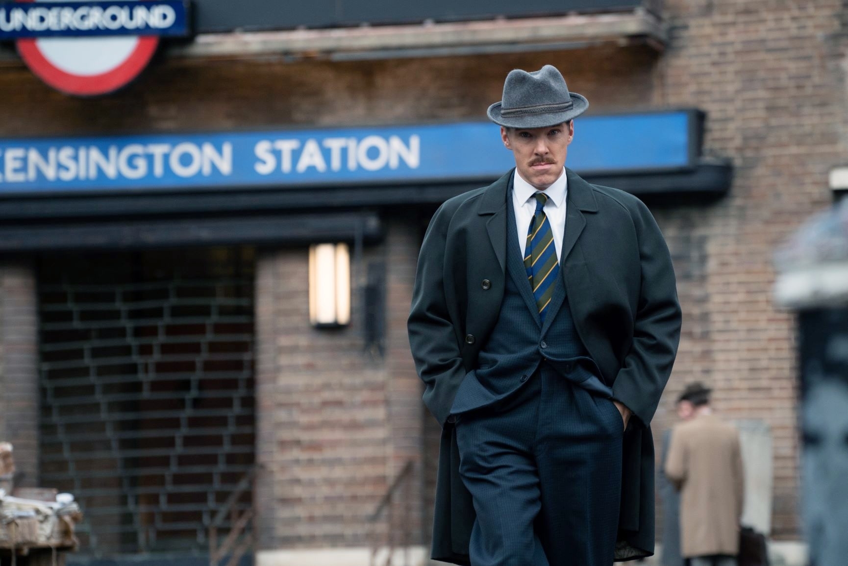 in a scene, Benedict in a coat and striped tie outside Kensington Station