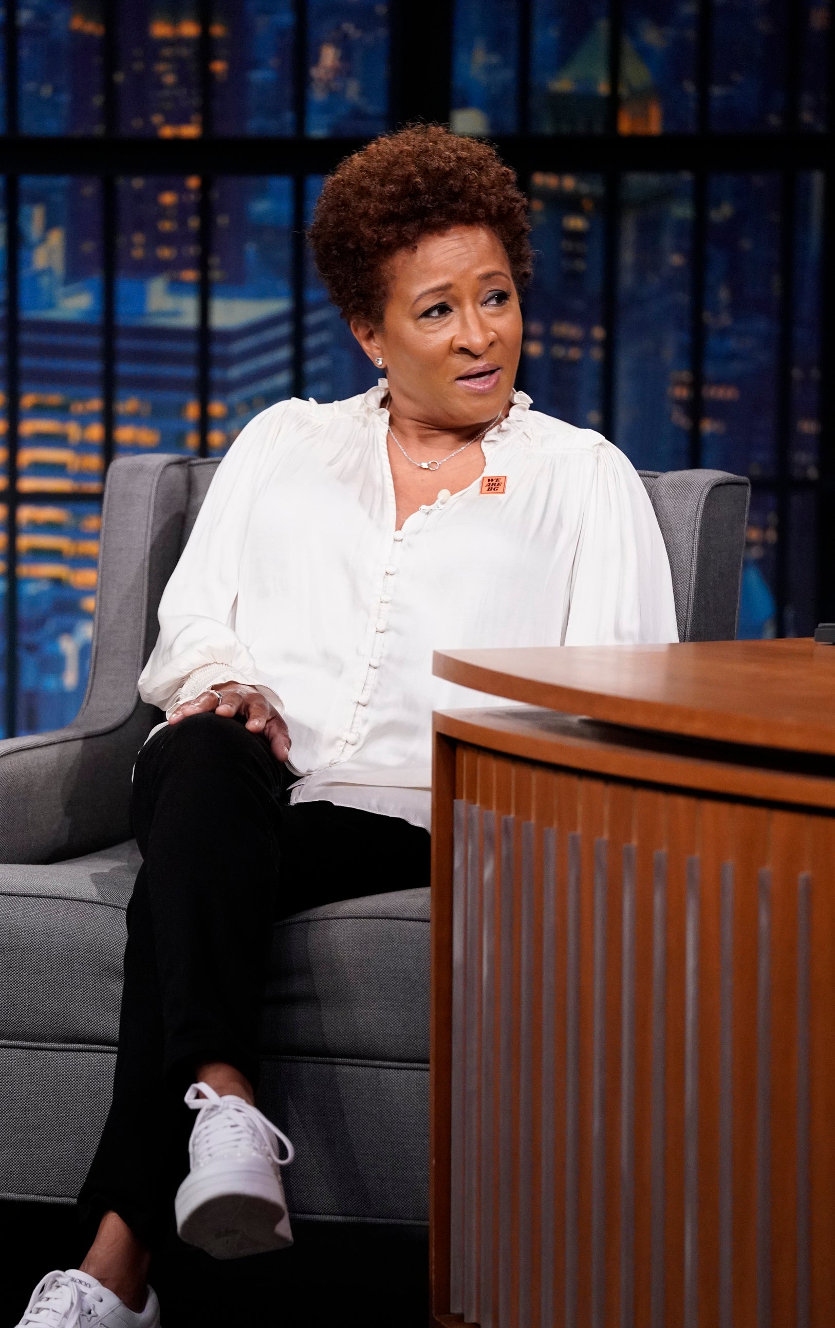 Wanda Sykes in a blouse and pants sits on a talk show chair, expressing a point
