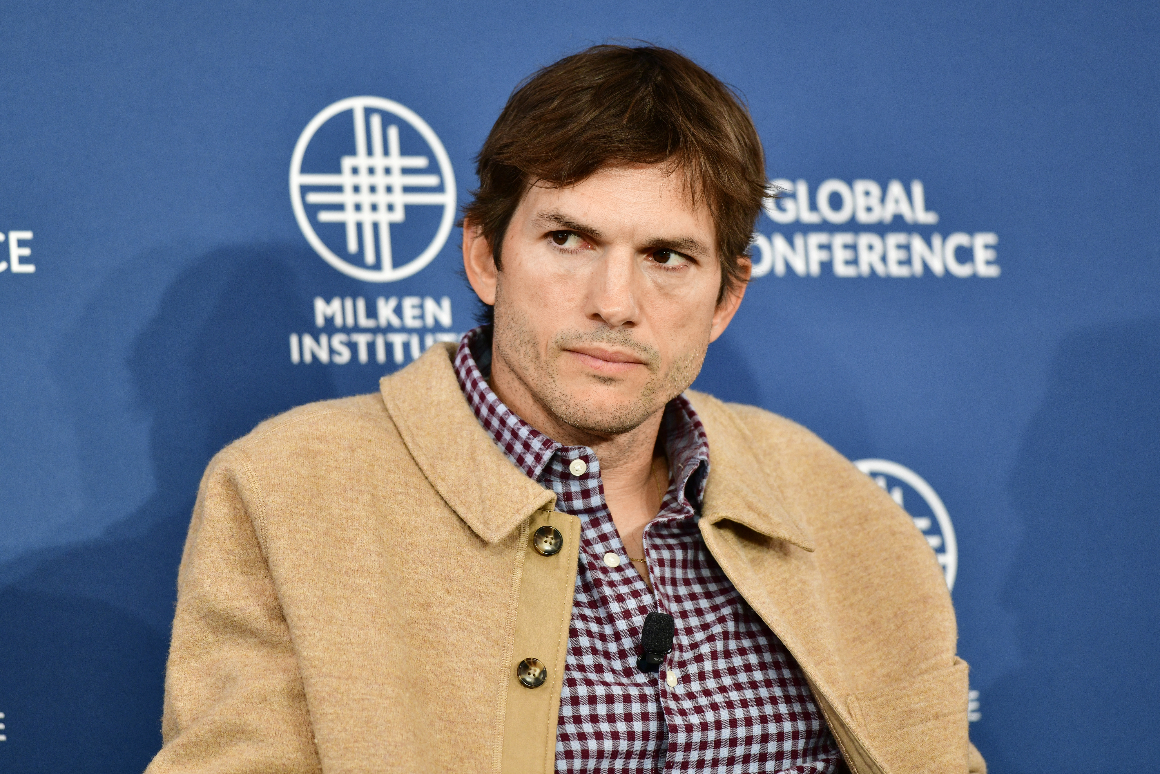 Ashton Kutcher in a jacket and plaid shirt at an event
