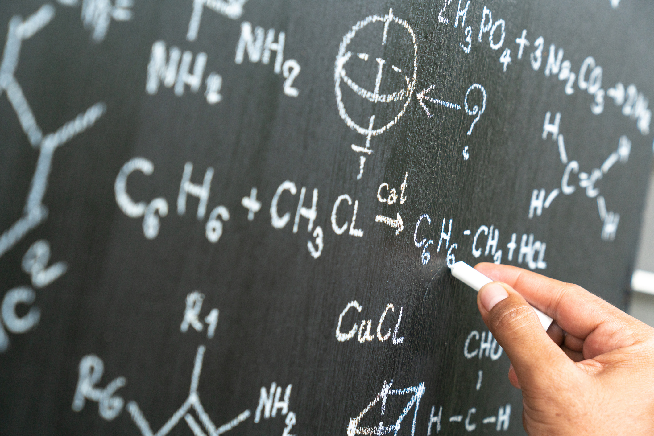Person writing chemical formulas on a blackboard with chalk
