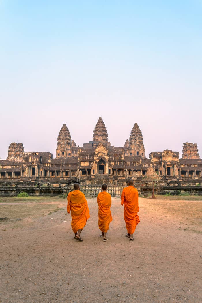 Three monks walking towards Angkor Wat temple at dawn