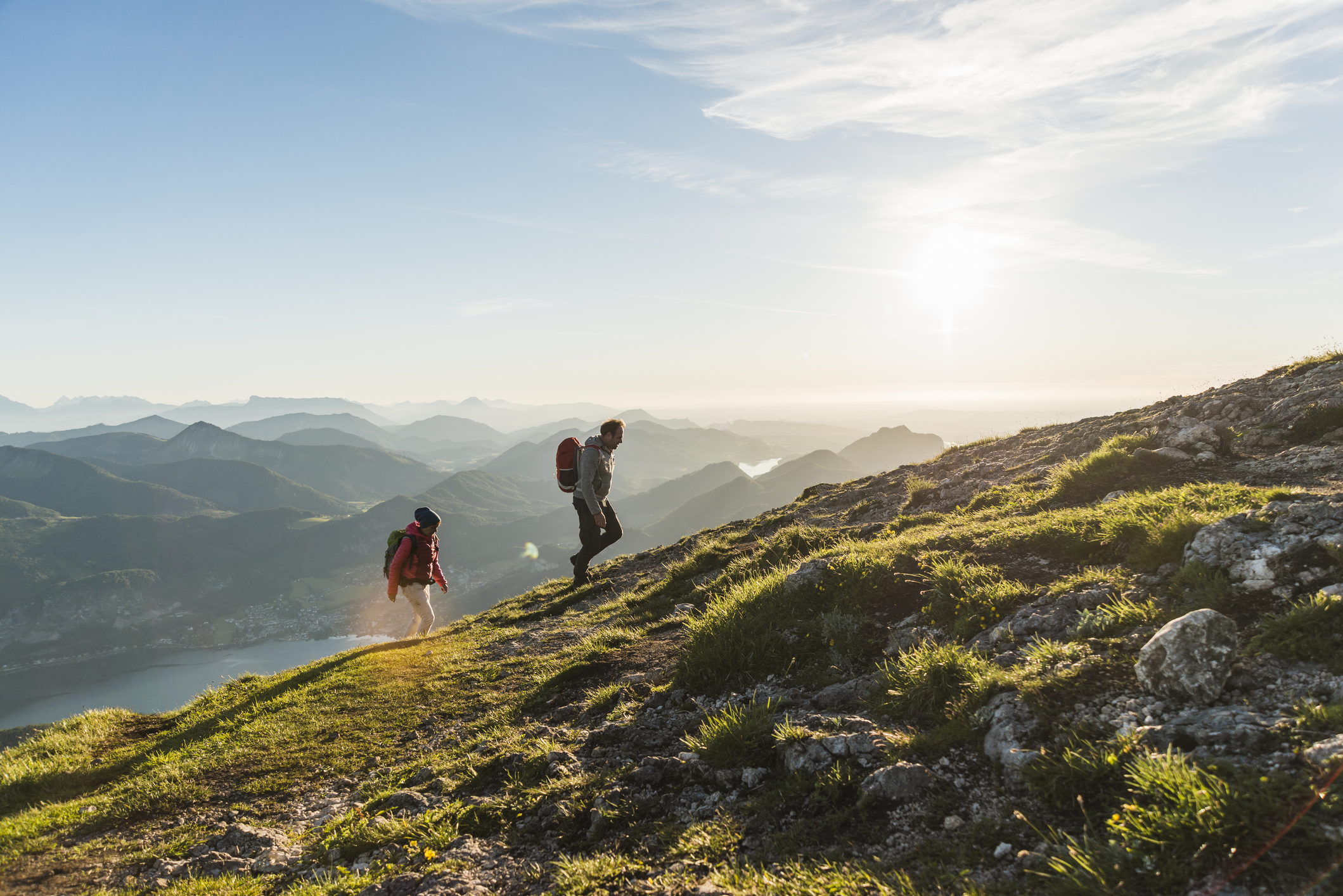 Two hikers with backpacks walking on a mountain trail at sunrise