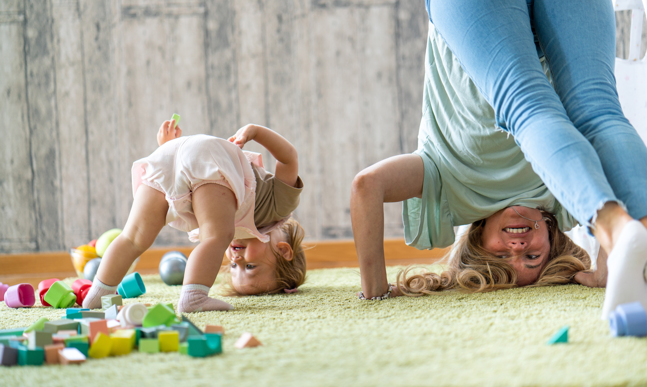 Adult and child playfully upside down indoors with toys scattered around