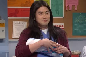Bowen Yang holding a baby in an SNL sketch