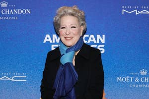 Bette Midler at an event wearing black coat, scarf, and gloves