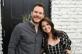 Two people smiling together against a white brick background. Man in a plaid shirt, woman in a checkered dress