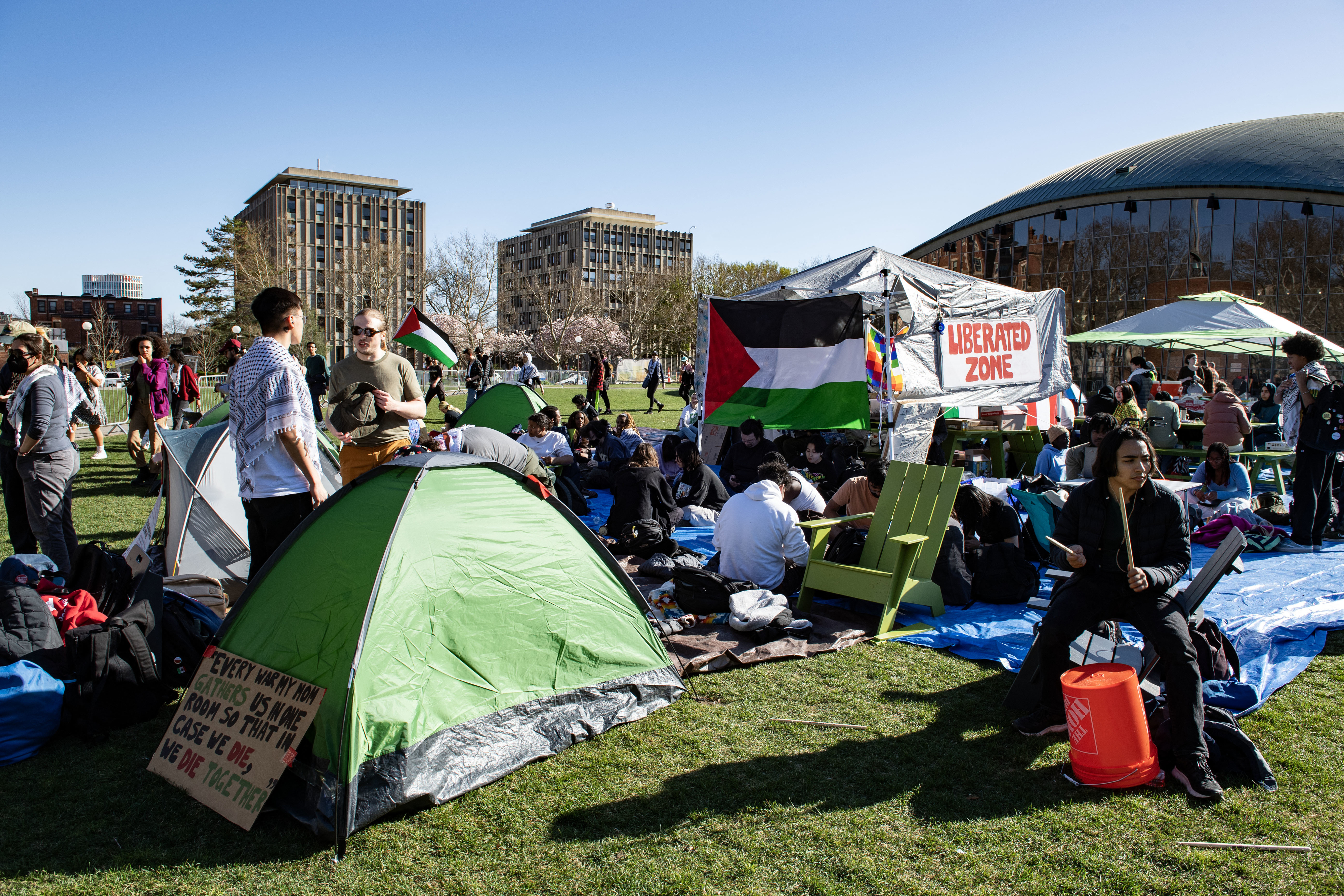 Group of people at an outdoor event with tents and a sign reading &quot;LIBERATED ZONE.&quot;