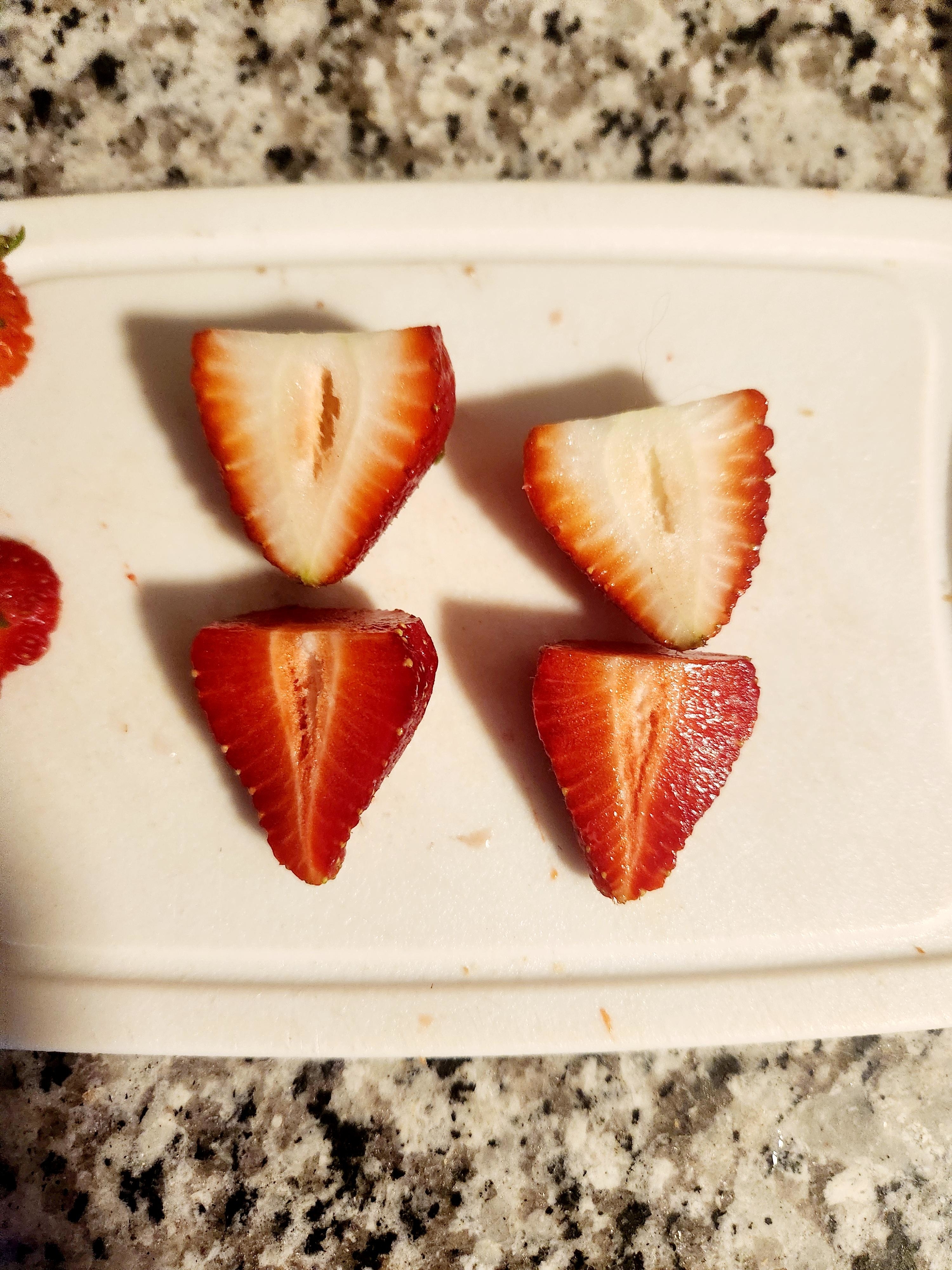 Four strawberry halves arranged in a diamond shape on a cutting board