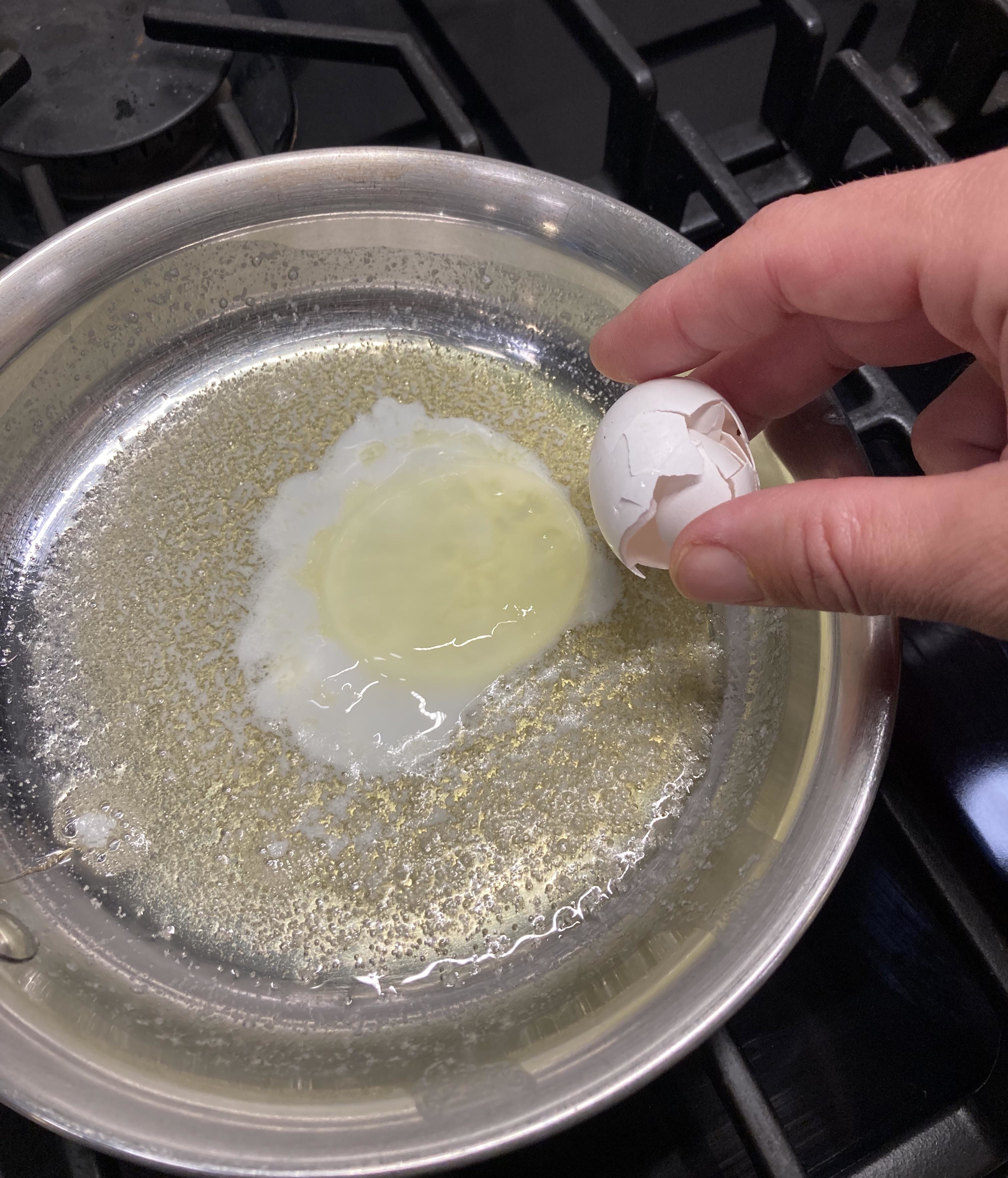 A person cracking an egg into a hot pan for cooking