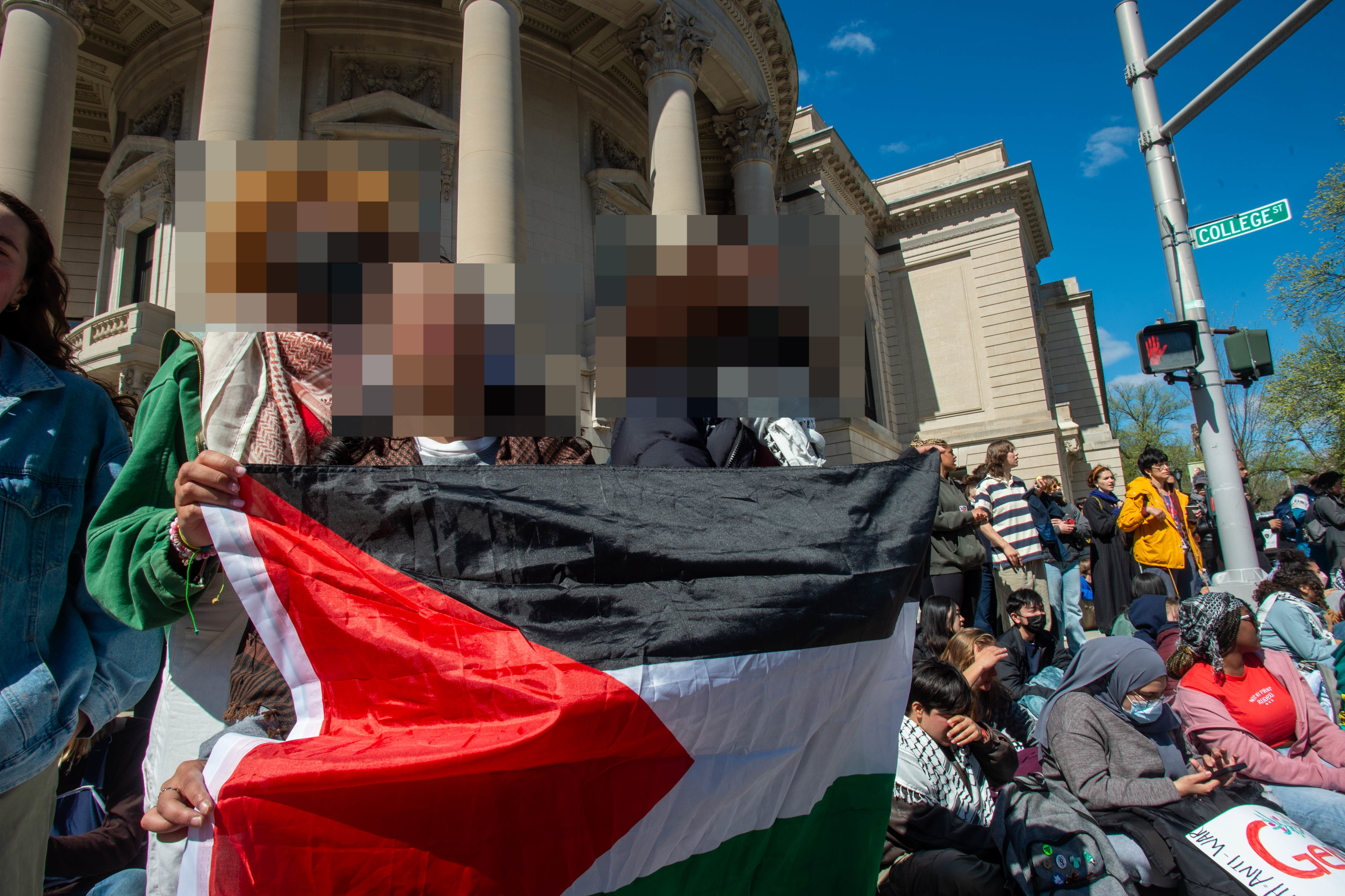 Protestors with a Palestinian flag in front of a building, expressing solidarity or demonstrating