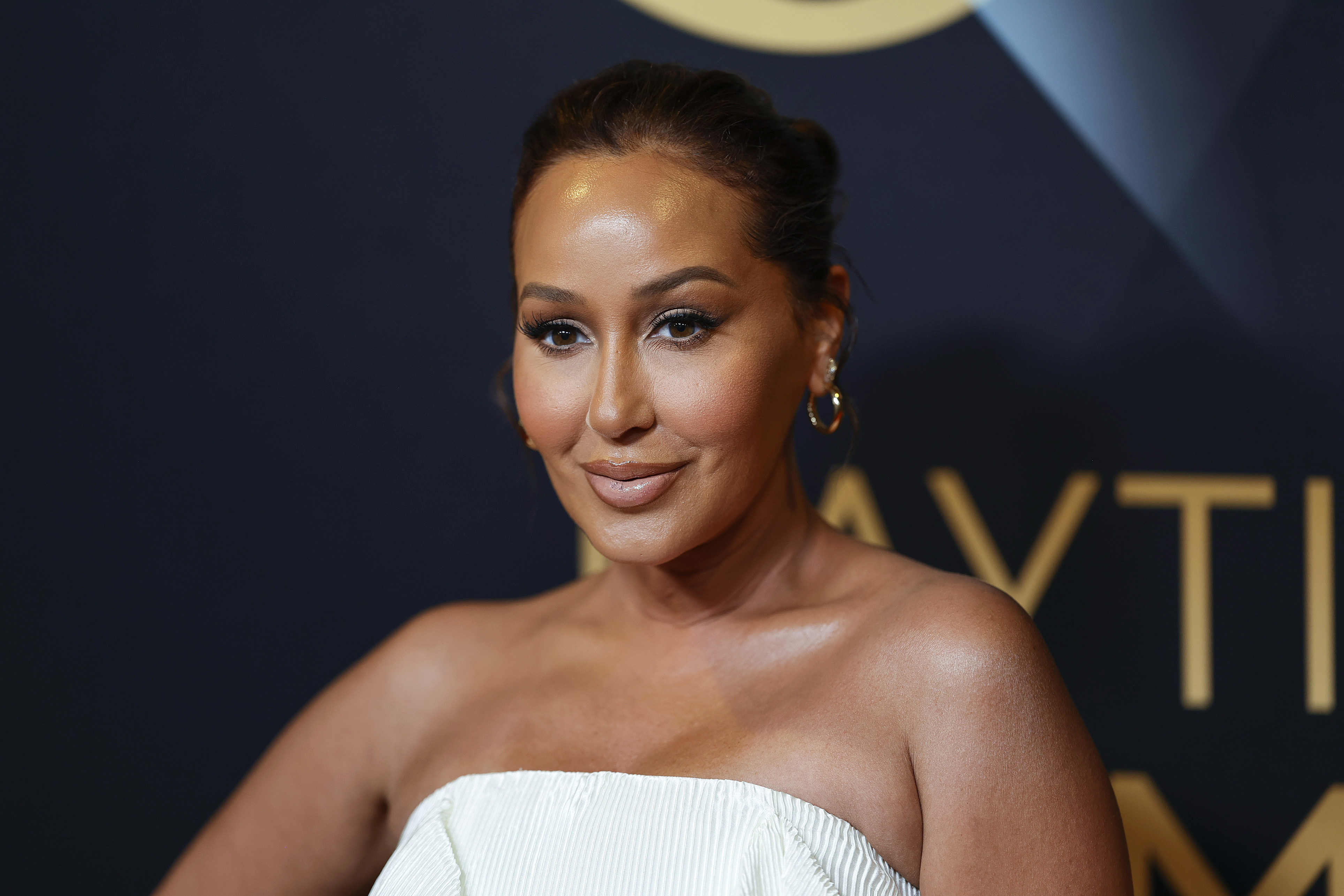 Adrienne Bailon posing in a off-shoulder dress and hoop earrings at an event