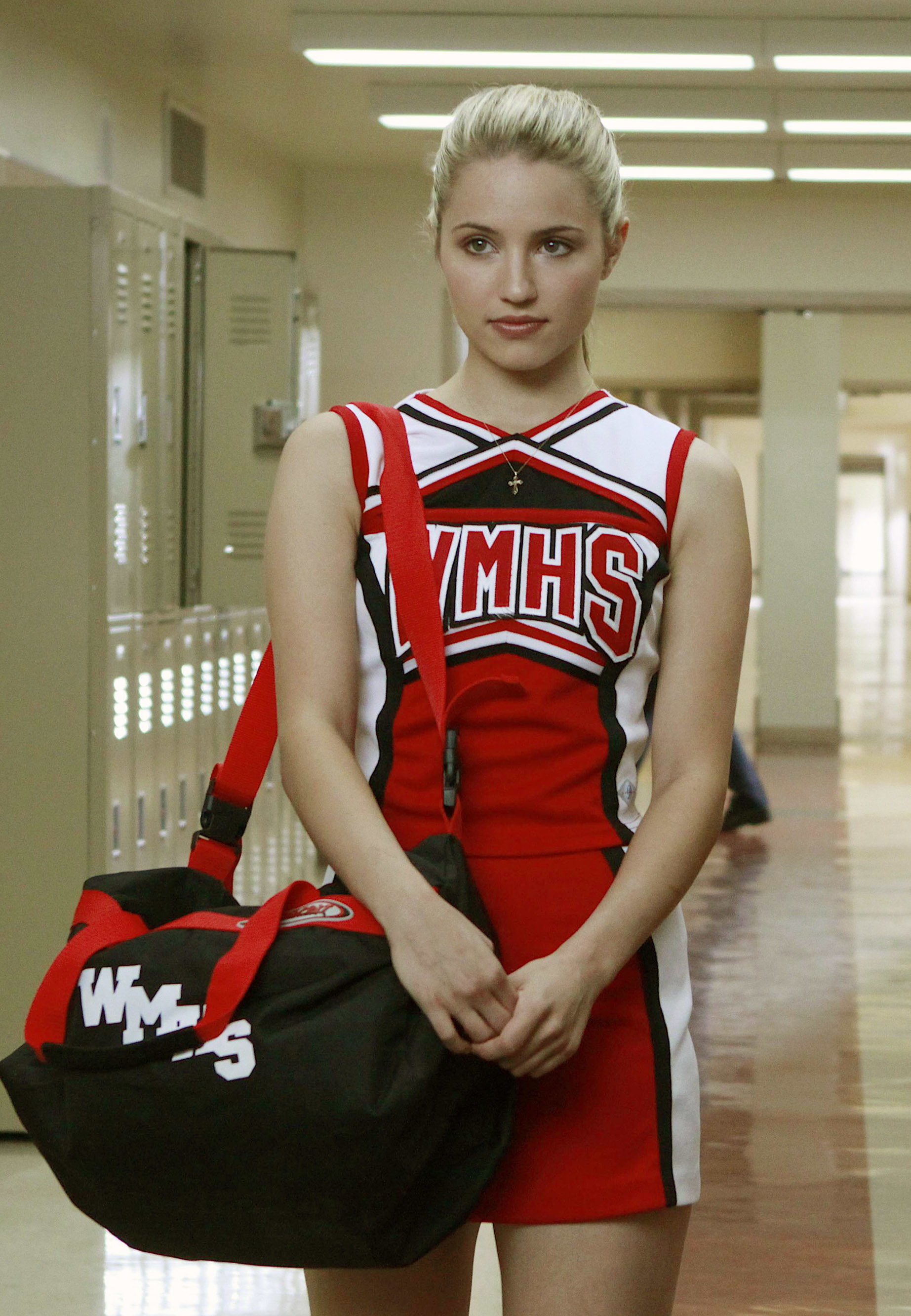 Quinn Fabray from Glee in a cheerleader uniform holding a gym bag, standing in a school hallway