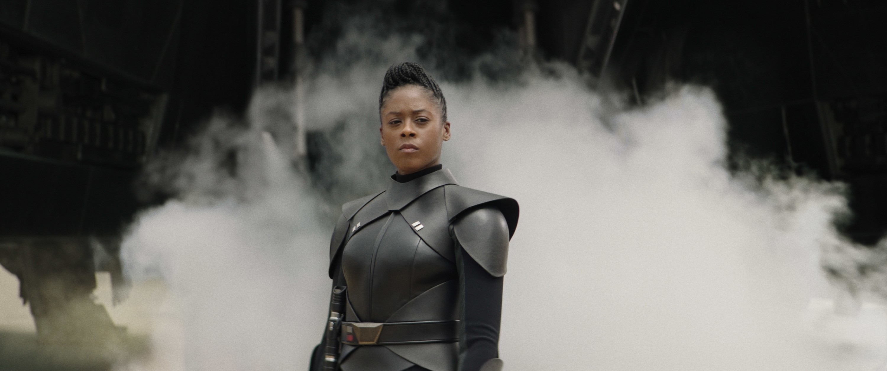 Character in a futuristic black outfit, standing confidently with a steely expression, smoke in the background