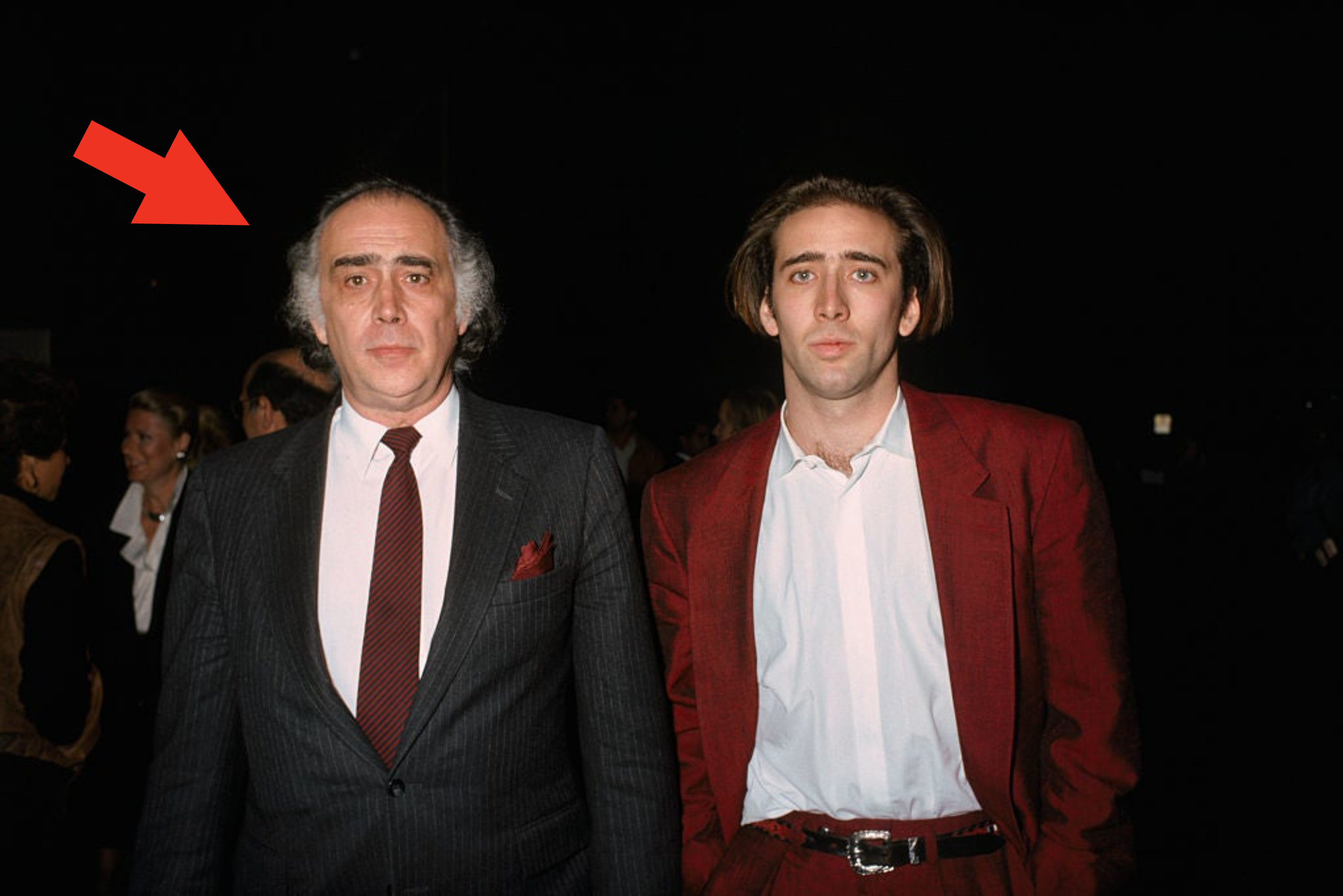 Two men at an event, one in a gray suit with a tie and the other in a red blazer over a white shirt