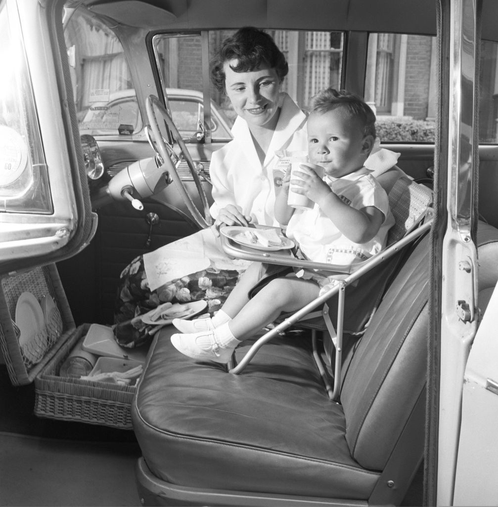 Woman feeding a child in a vintage car&#x27;s front seat with tray