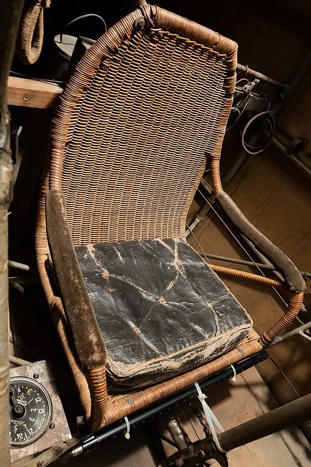Worn-out wicker chair with a torn black seat, set in a rustic room with vintage objects