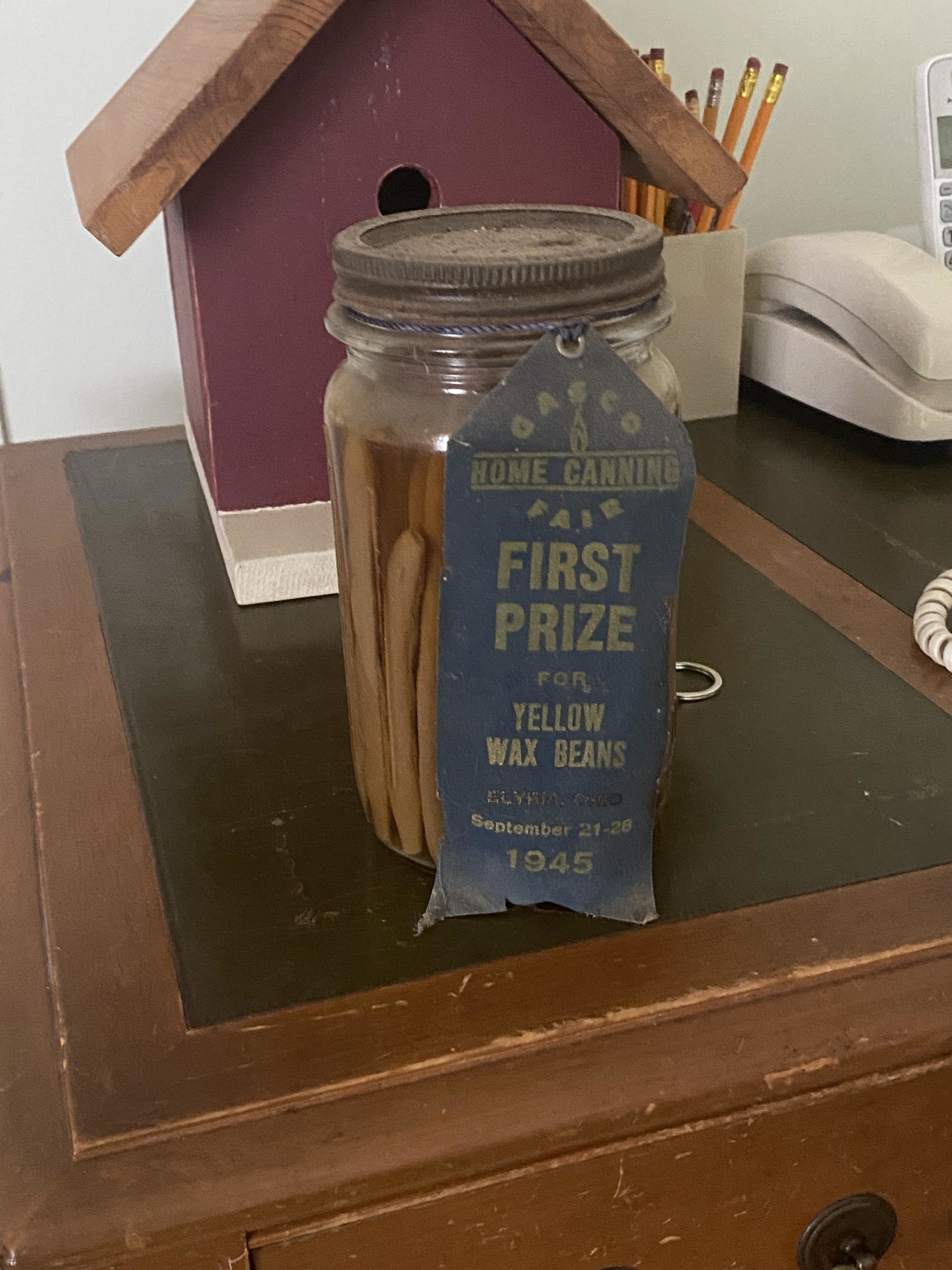 Jar of yellow wax beans with a &#x27;First Prize&#x27; ribbon from a 1945 canning fair on a wooden surface
