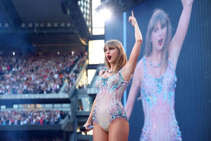 Taylor Swift performing on stage in a sparkly bodysuit with a crowd in the background
