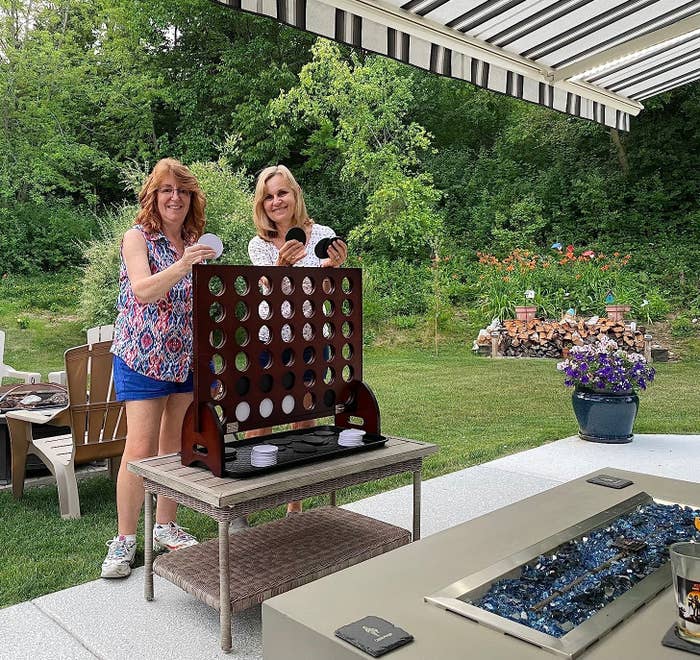 Two women playing a large outdoor Connect Four game on a patio