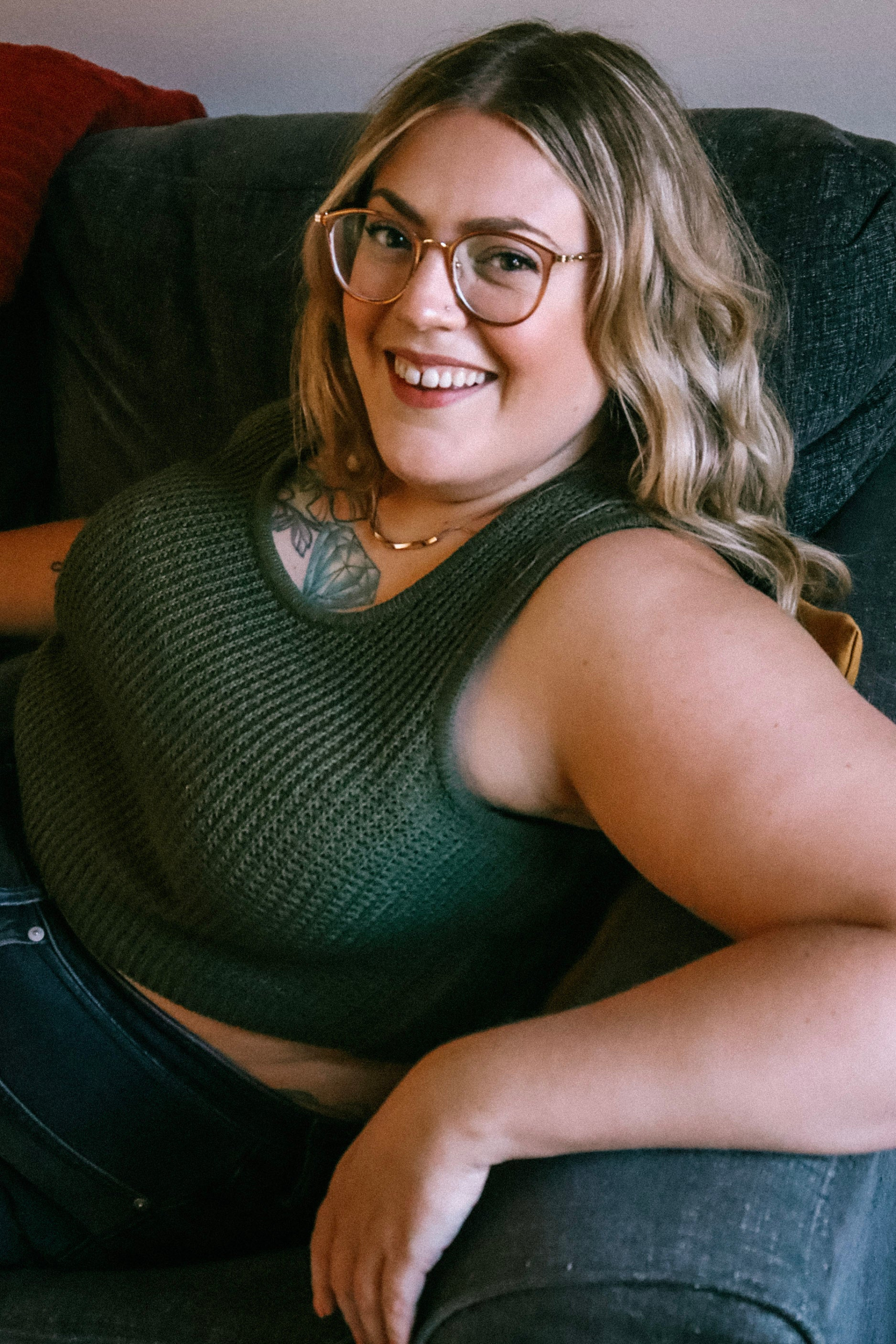 Karli in glasses and green top lounging on a sofa, smiling at the camera