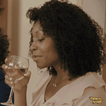 Woman with curly hair holding a wine glass, smiling, and making a toast gesture