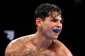 Boxer with mouthguard visible, tattoos on chest and arms, wet hair, in the ring