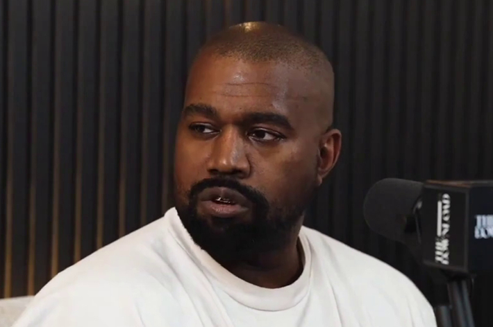 Kanye West in a white top during an interview, with a microphone in the foreground