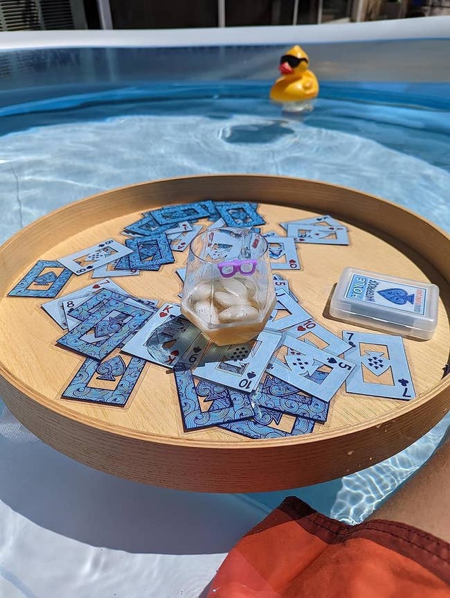 Playing cards scattered connected a woody tray successful a pool, with a rubber duck nearby
