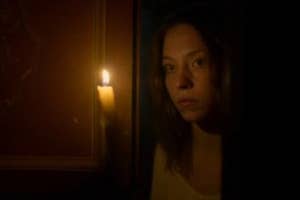 Woman holding a candle, looking intently, in a dimly lit room