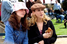Charlotte in a pink bucket hat, Carrie in a brown beret, both engaged in conversation while sitting on a park bench.