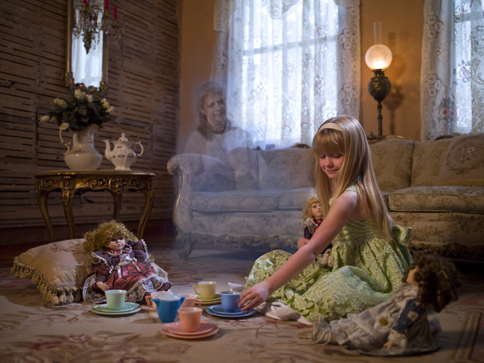 Child playing tea party with dolls, ghostly figure in background._interaction and imagined presence