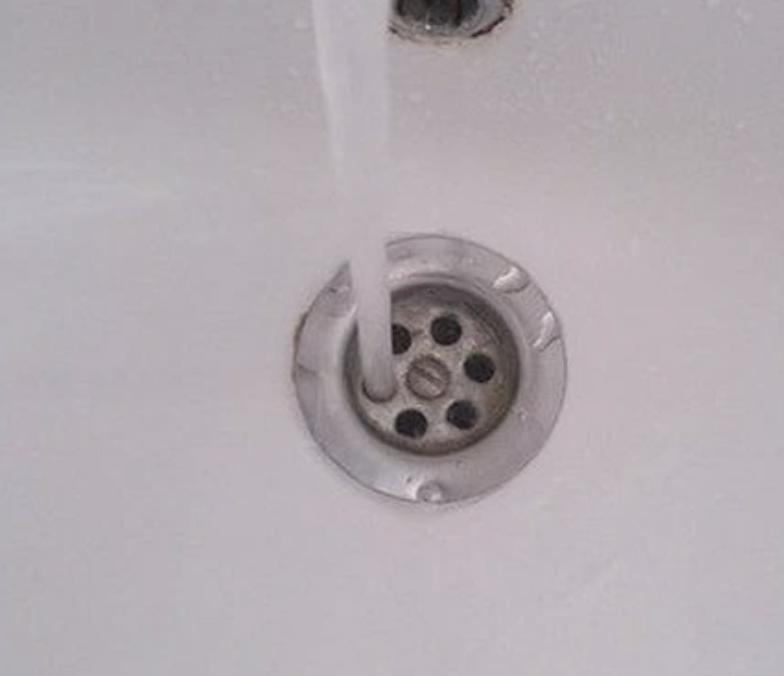 Water flowing into a sink through the drain with a visible clog catcher