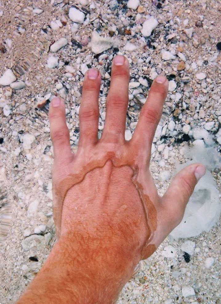 Hand with a clear water-outline on skin, resting on sandy beach showing a temporary imprint