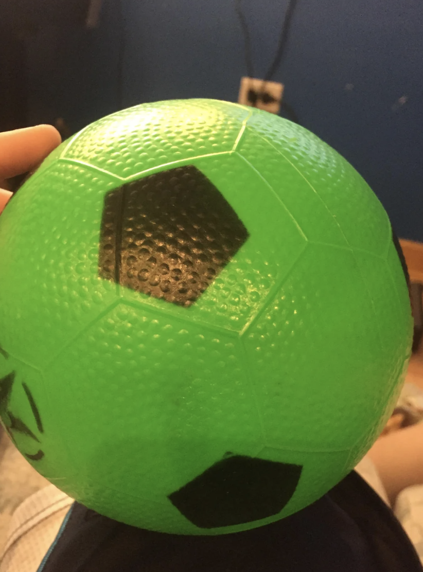 Person holding a textured green soccer ball with black patches