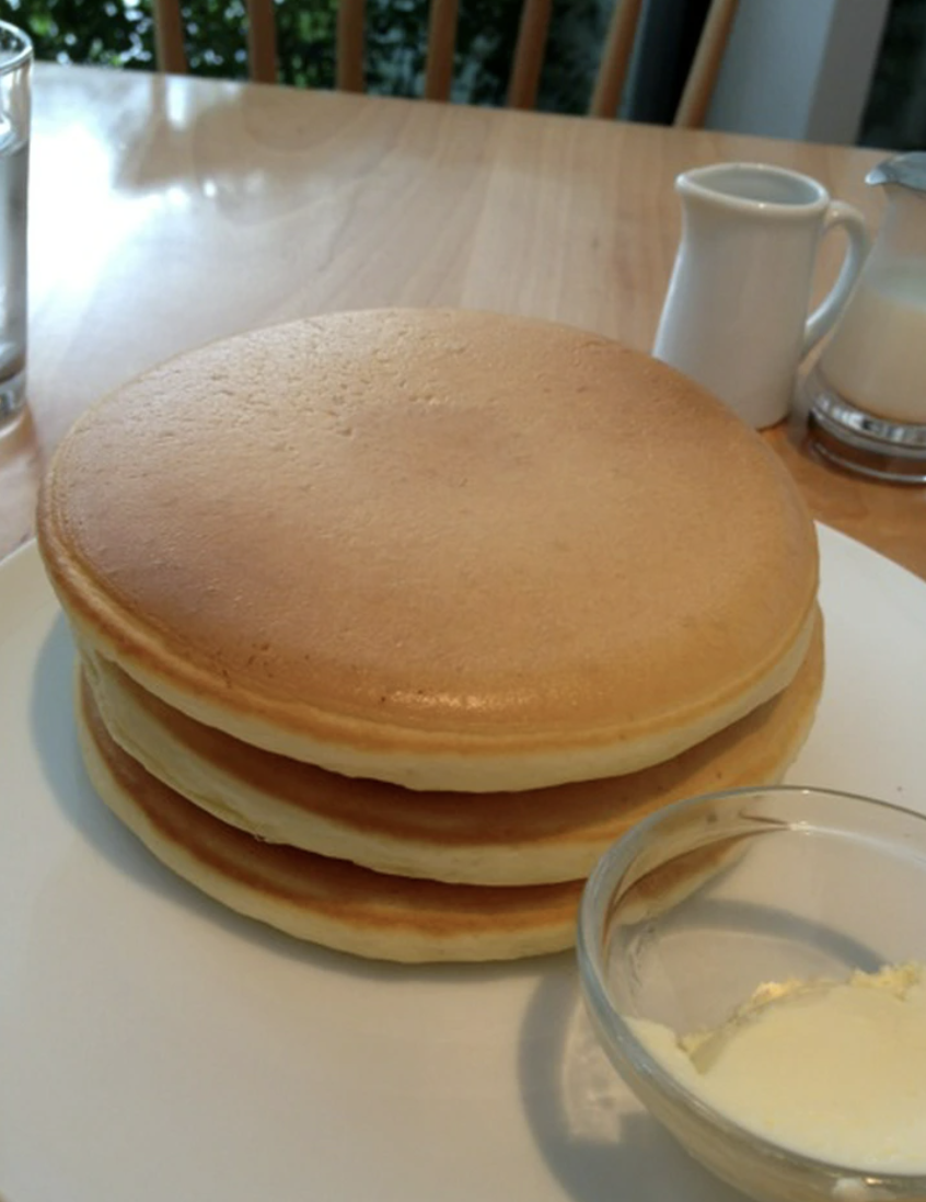 A stack of fluffy pancakes on a plate with butter and syrup on the side