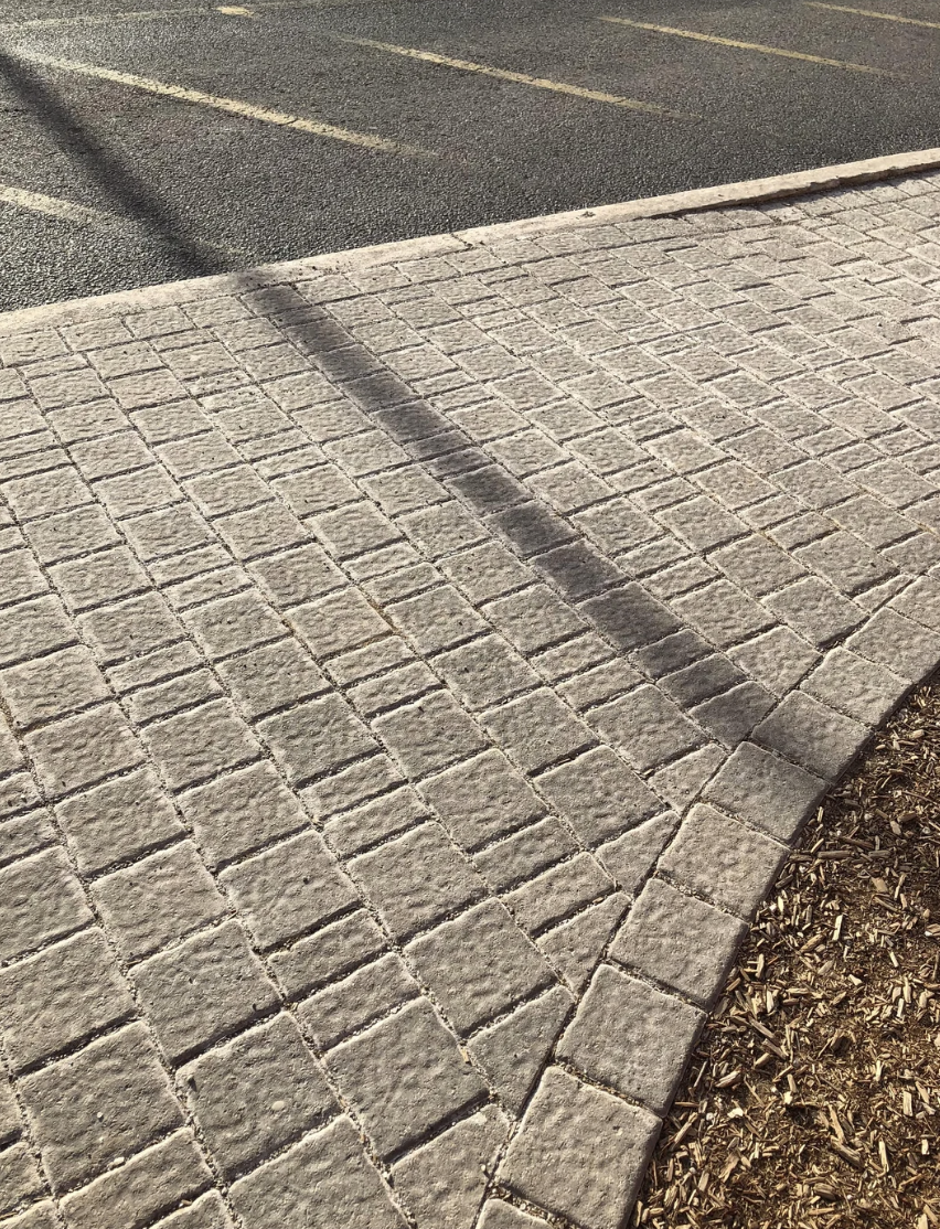 Tactile paving at a curb ramp with shadows crossing over