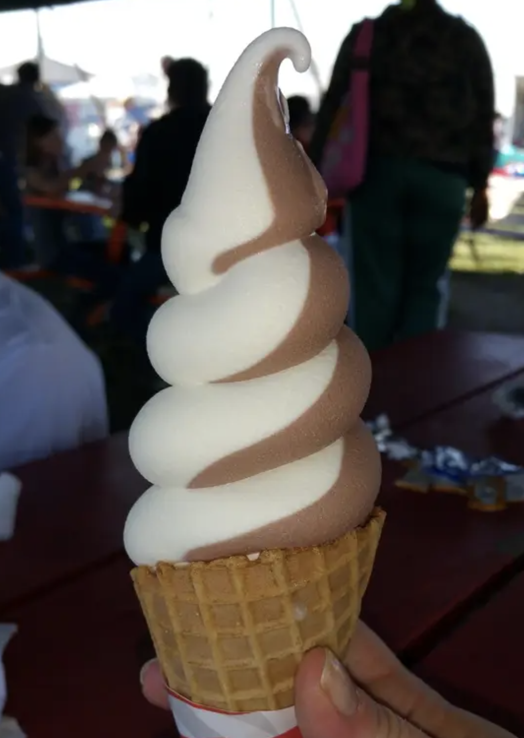 Person holding a twist of vanilla and chocolate soft serve ice cream in a waffle cone