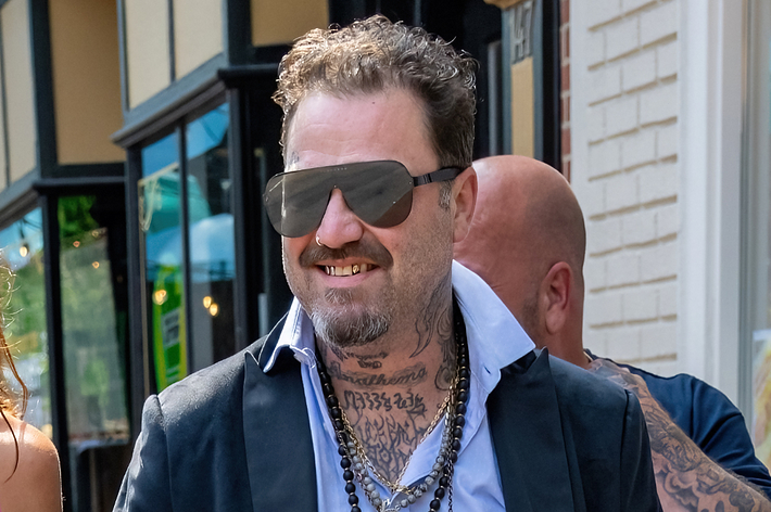 Bam Margera in sunglasses and tattooed, wearing a casual black outfit, walking outside