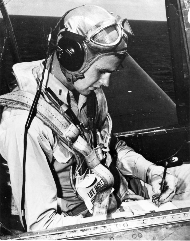 Pilot in cockpit with headset and life jacket writing on a clipboard