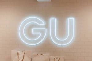 壁に取り付けられた「GU」というネオンサインの上部が写っている。周囲はショッピングバッグで飾られている。